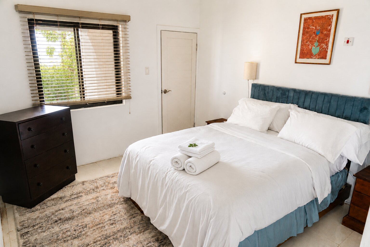 The Copperwood bedroom, bright with crisp white bedding and a blue upholstered headboard